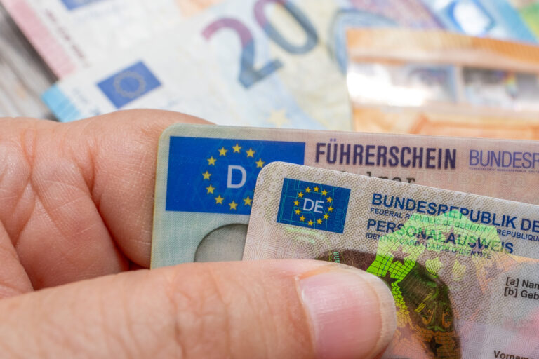 Close-up of a hand holding multiple Euro banknotes, showing a 50-euro note and other colorful bills.